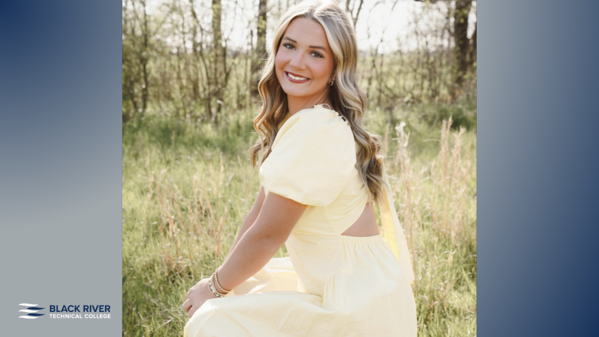 A young woman with long wavy blonde hair, wearing a pale yellow dress, smiles over her shoulder while kneeling in a grassy field, with Black River Technical College branding.